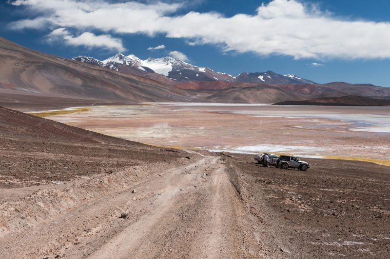Camioneta en un camino de ripio de la Puna, con salar y picos nevados